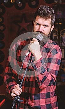 Man with calm face holds microphone, singing song, black background. Guy likes to sing rock songs. Musician with beard