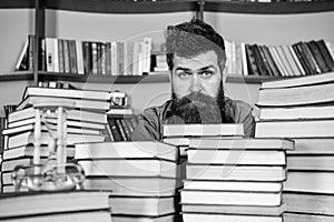 Man on calm face between piles of books, while studying in library, bookshelves on background. Bibliophile concept