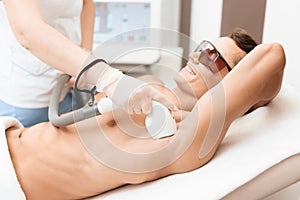 The man came to the procedure of laser hair removal. The doctor treats his armpit with a special apparatus. photo
