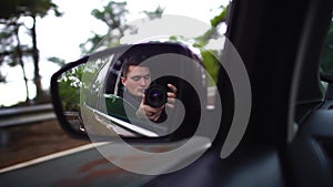 Man with camera in car mirror reflection of a moving car along autumn foggy road during morning journey. Slow motion.