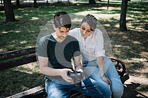 Man with camera sitting on bench next to girl and checking images