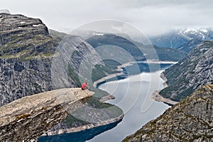 Man with camera sitting on Trolltunga rock and makes the photo with the Norwegian mountain landscape