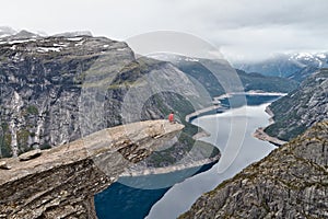 Man with camera sitting on Trolltunga rock Troll`s Tongue rock