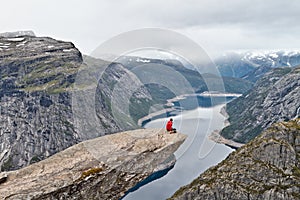 Man with camera sitting on Trolltunga rock Troll`s Tongue rock