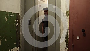 Man in cap with backpack walk out narrow elevator. Old house. Ragged walls