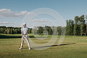 Man in cap holding golf club and hitting ball on green lawn