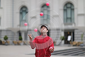 A man in a cap juggles with pink balls on a stree