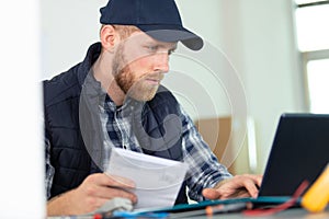 man in cap reading instructions and using laptop computer