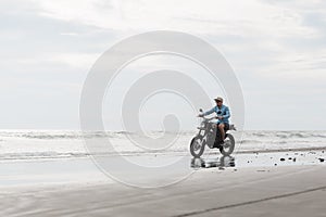 Man in cap riding motorcycle on beach. Moto cross dirtbiker on beach sunset on Bali. Young hipster male enjoying freedom