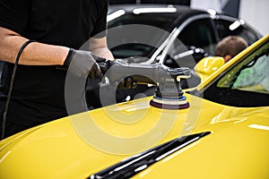 Man car detailing studio worker polishing yellow car varnish with electrical polisher