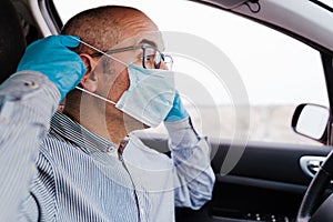 Man in a car putting on protective mask and gloves during pandemic coronacirus covid-19