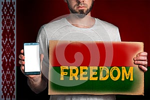 A man with a cardboard and a phone in his hand. The Flag Belarus. Concept of freedoms and human rights. Text freedom