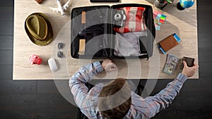 Man carefully packing suitcase for travel, taking money and documents, top view