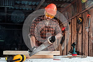 A man carpenter cuts a wooden beam using a handsaw, male hands with a saw closeup. Work with wood