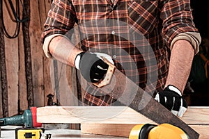 A man carpenter cuts a wooden beam using a handsaw, male hands with a saw closeup. Work with wood