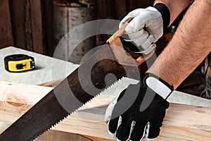 A man carpenter cuts a wooden beam using a handsaw, male hands with a saw closeup. Work with wood