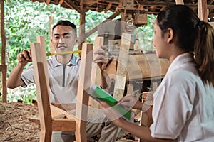 Man carpenter measuring wood using ribbon ruler and business woman using tablet pc