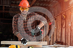 A man carpenter twists a screw into a tree with an electric screwdriver, male hands with a screwdriver close-up. Work with wood