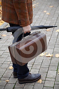 Man with carpetbag in jacket stands in alley of autumn park