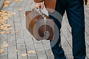 Man with carpetbag in jacket stands in alley of autumn park