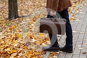 Man with carpetbag in jacket stands in alley of autumn park