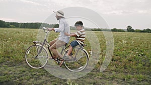 A man carries a child on a retro bike. Father and son are driving through a flower field. Retro style. A fashionable bicycle