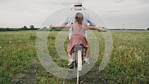 A man carries a child on a retro bike. a man and a girl are driving through a flower field. Retro style. A fashionable bicycle