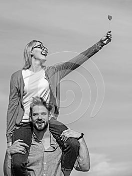 Man carries girlfriend on shoulders, sky background. Couple happy date having fun together. Woman holds heart on stick