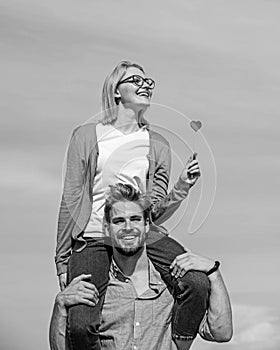 Man carries girlfriend on shoulders, sky background. Couple happy date having fun together. Woman holds heart on stick