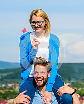 Man carries girlfriend on shoulders, sky background. Romantic date concept. Woman holds heart on stick symbol of love