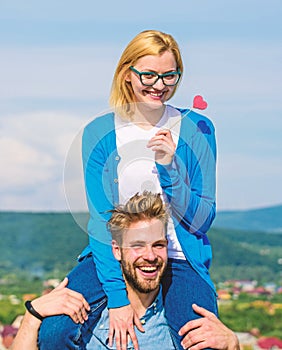 Man carries girlfriend on shoulders, sky background. Romantic date concept. Woman holds heart on stick symbol of love