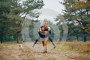 Man carries his wife and daughter on his back at forest path next to dog during walk