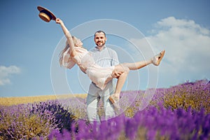 A man carries his woman in his arms through a lavender field, love, romantic relationships, the girl rejoices. Beautiful blonde in photo