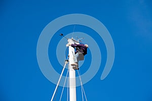 A man carries out work on the top of the mast of a sailboat