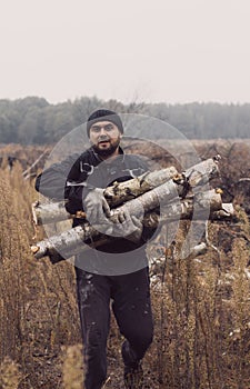 A man carries a pile in two hands. Front view, looking at the camera. A Caucasian man has cut logs for firewood and