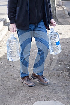 The man carries two bottles of drinking water