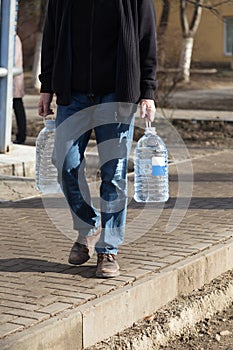 The man carries two bottles of drinking water