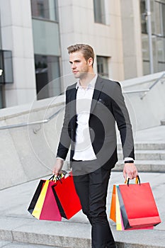 Man carry shopping bags on urban backdrop. Businessman with package walk in street. Fashion shopper with paperbags
