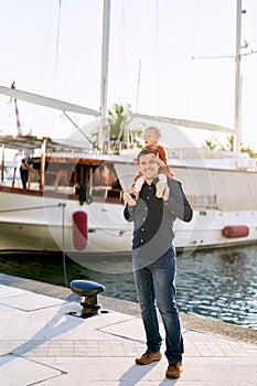 Man is carrying his daughter on his shoulders on a boat pier by the sea