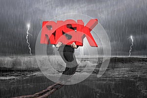 Man carrying red RISK word on chain with stormy ocean