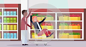 Man carrying trolley cart with woman happy mix race couple having fun supermarket interior shopping concept male female