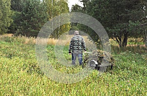 A man is carrying a trolley with mown grass