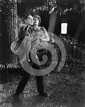 Man carrying a woman in his arms through a backyard