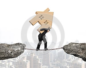 Man carrying wooden house balancing on chain connected cliffs