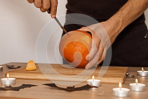 A man carves eyes and a mouth in a pumpkin for Halloween.