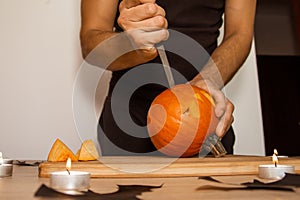 A man carves eyes and a mouth in a pumpkin for Halloween.