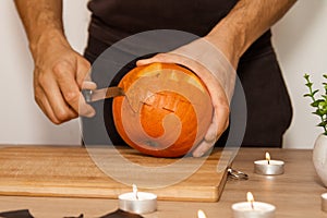 A man carves eyes and a mouth in a pumpkin for Halloween.