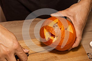 A man carves eyes and a mouth in a pumpkin for Halloween.