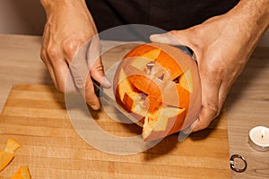 A man carves eyes and a mouth in a pumpkin for Halloween.