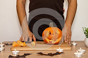 A man carves eyes and a mouth in a pumpkin for Halloween.